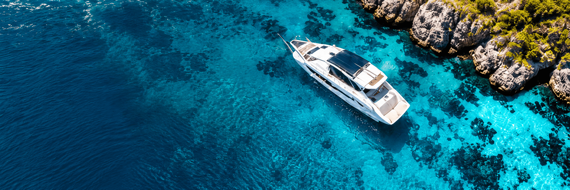 White luxury yacht over clear turquoise water beside a rocky coastline